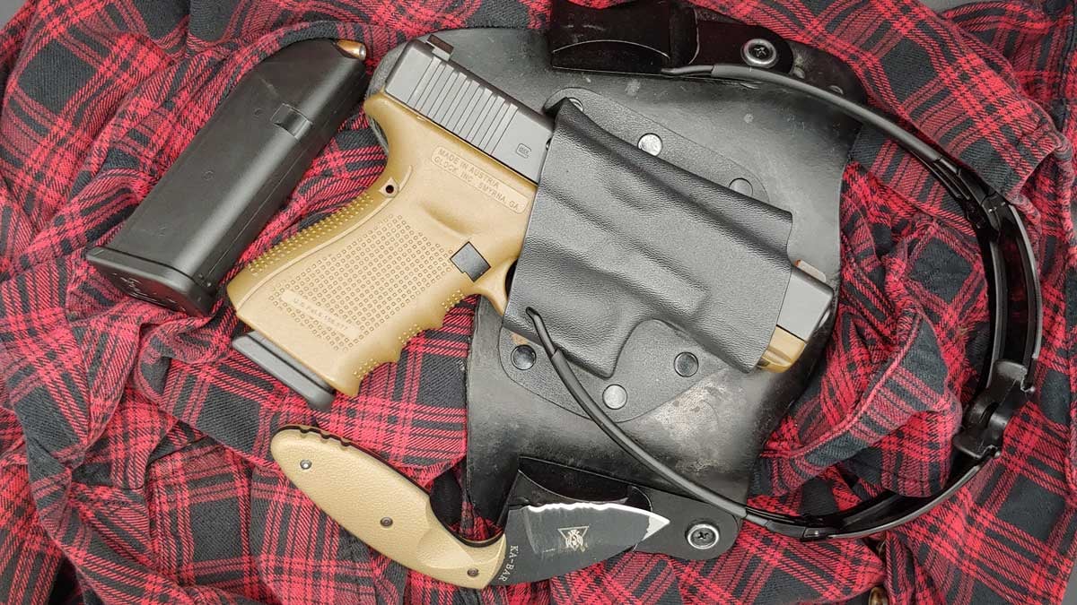 glock g19 in a leather holster next to spare magazine and a knife