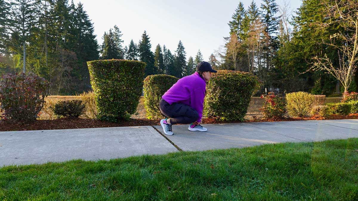 Woman tying running shoes on sidewalk