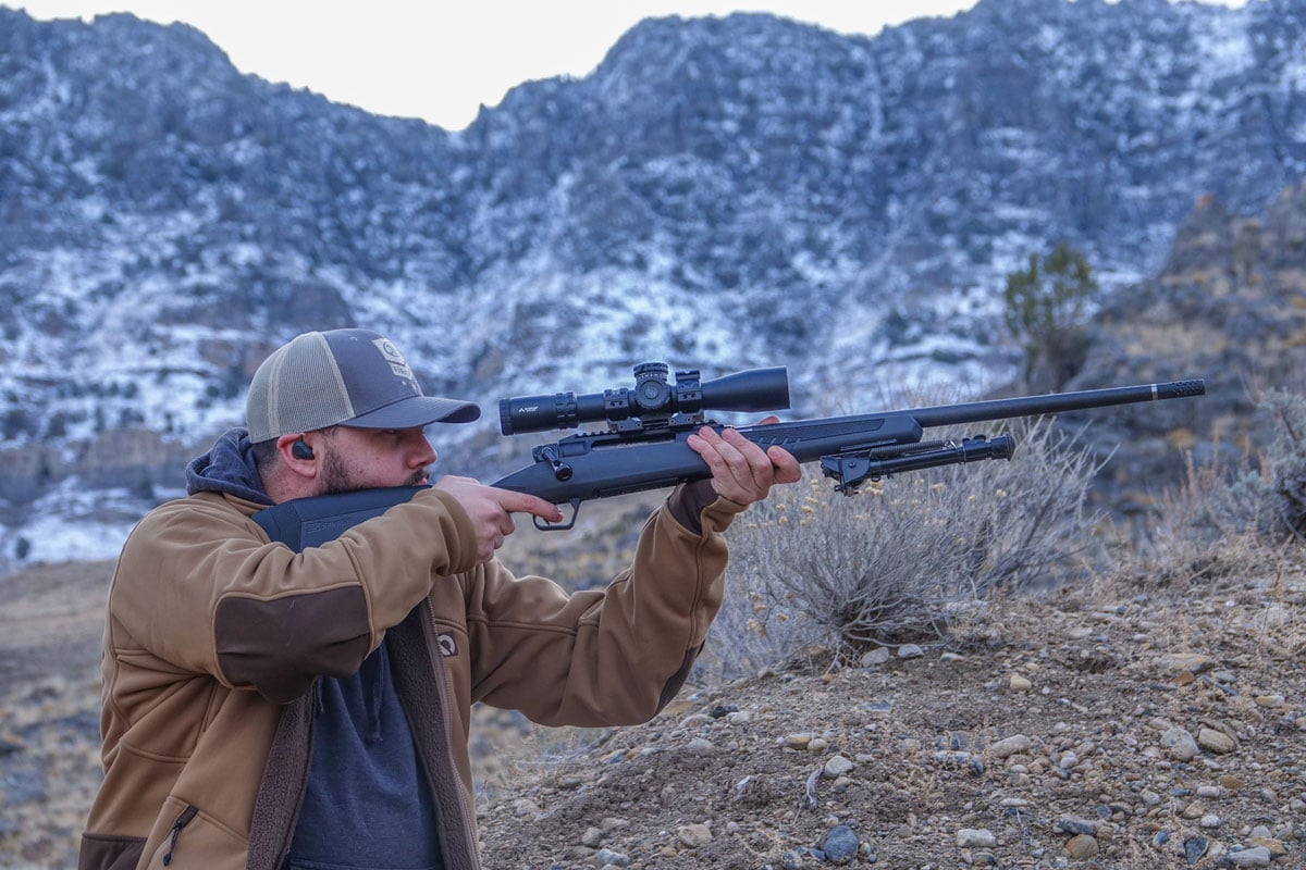 man aiming rifle while standing in desert