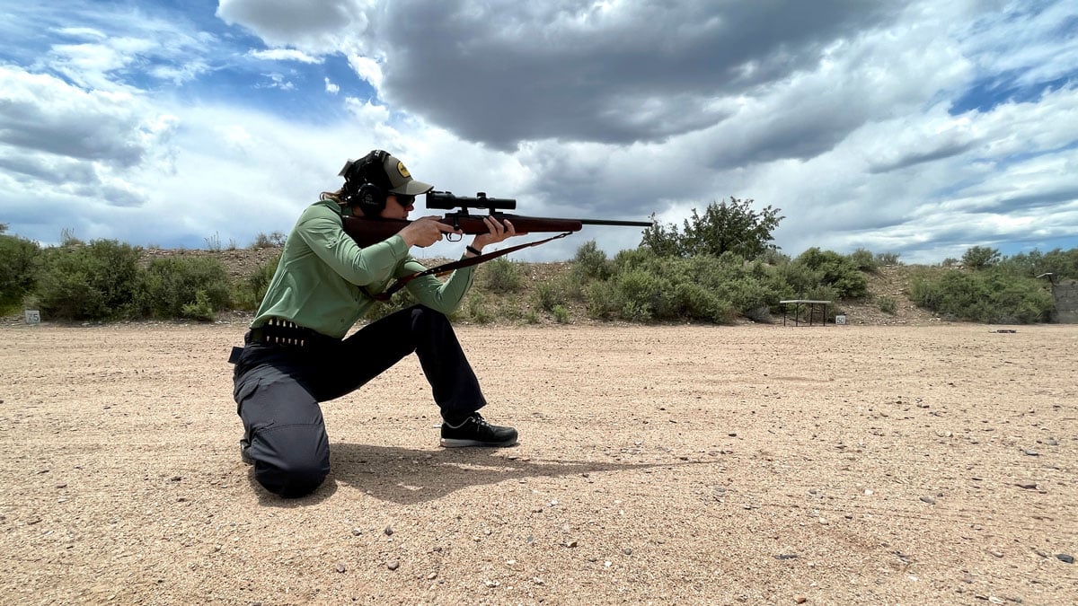 woman aiming rifle in braced kneeling position