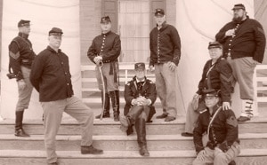 Reenactors standing the on the steps of a building posing in Confederate uniforms.